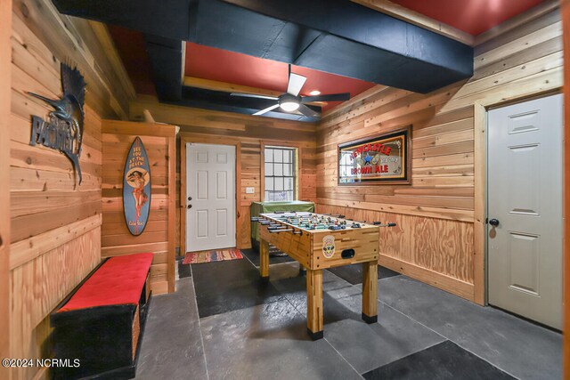 game room with wood walls, ceiling fan, and concrete flooring