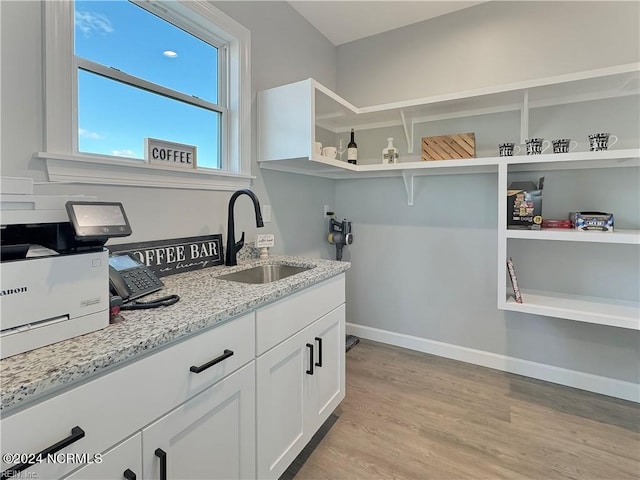 kitchen with light stone countertops, sink, white cabinetry, and light hardwood / wood-style floors