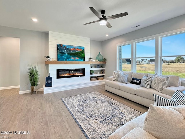 living room with a large fireplace, light hardwood / wood-style floors, and ceiling fan