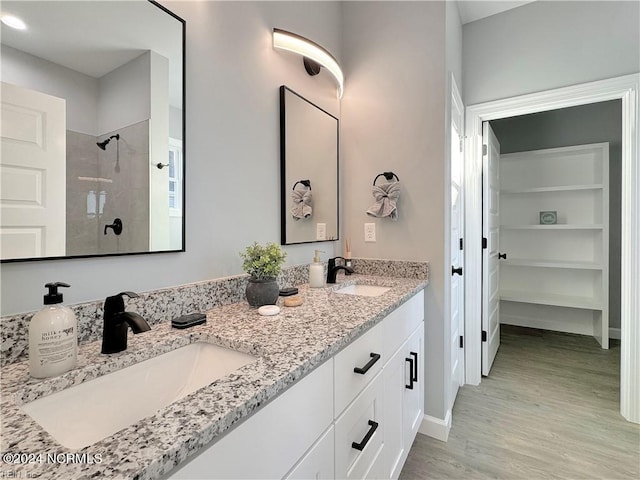 bathroom featuring tiled shower, wood-type flooring, and dual bowl vanity