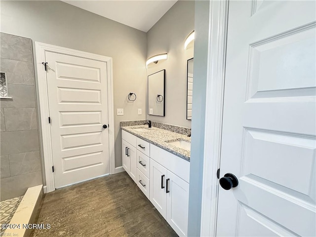 bathroom with a tile shower, double sink vanity, and hardwood / wood-style flooring