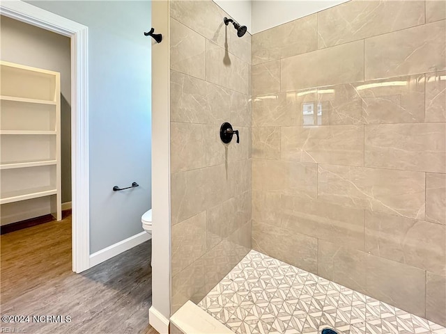 bathroom with toilet, tiled shower, and wood-type flooring