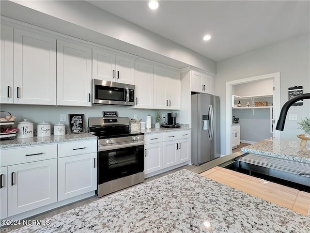 kitchen featuring light wood-type flooring, stainless steel appliances, sink, light stone countertops, and white cabinets