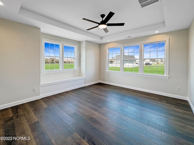 empty room featuring dark hardwood / wood-style flooring, ceiling fan, and a tray ceiling