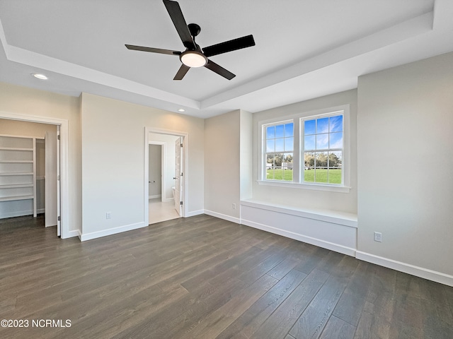 unfurnished bedroom featuring dark hardwood / wood-style flooring, ceiling fan, a tray ceiling, and ensuite bath