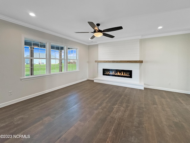 unfurnished living room featuring dark hardwood / wood-style flooring, ceiling fan, ornamental molding, and a large fireplace