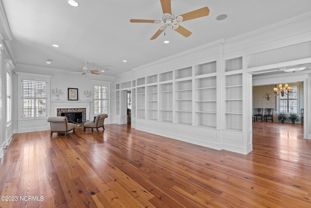 unfurnished room with dark wood-type flooring, plenty of natural light, a fireplace, ceiling fan with notable chandelier, and crown molding