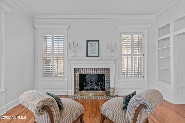 living area featuring built in features, ornamental molding, wood-type flooring, and a fireplace