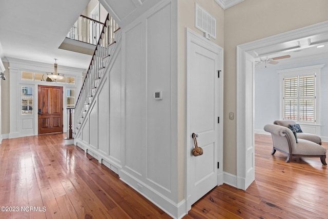 foyer with hardwood / wood-style floors, ceiling fan with notable chandelier, and ornamental molding