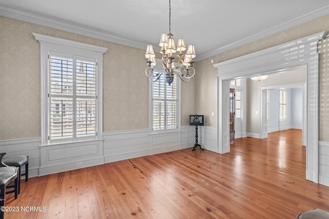 empty room featuring plenty of natural light, crown molding, light wood-type flooring, and an inviting chandelier