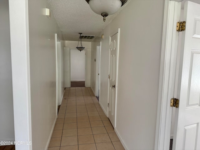 corridor with a textured ceiling and light tile floors