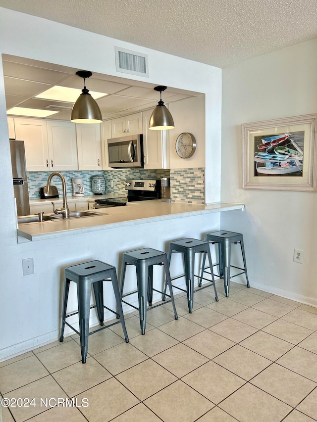 kitchen with a kitchen bar, hanging light fixtures, appliances with stainless steel finishes, and backsplash