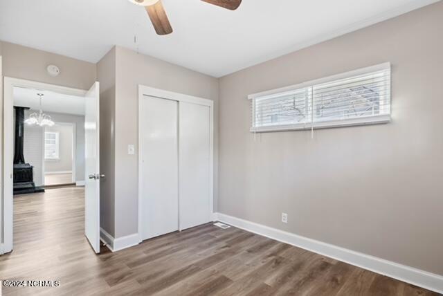 unfurnished bedroom featuring ceiling fan with notable chandelier, hardwood / wood-style flooring, and a closet