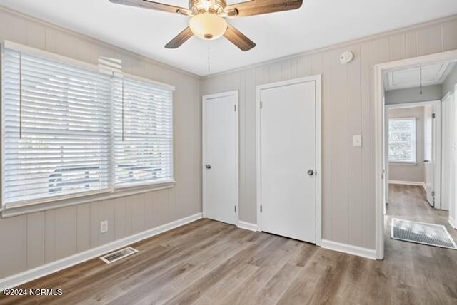 unfurnished bedroom featuring ceiling fan, crown molding, light hardwood / wood-style floors, and multiple windows