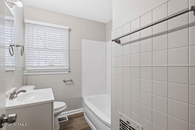 full bathroom with tiled shower / bath combo, hardwood / wood-style flooring, toilet, vanity, and tile walls