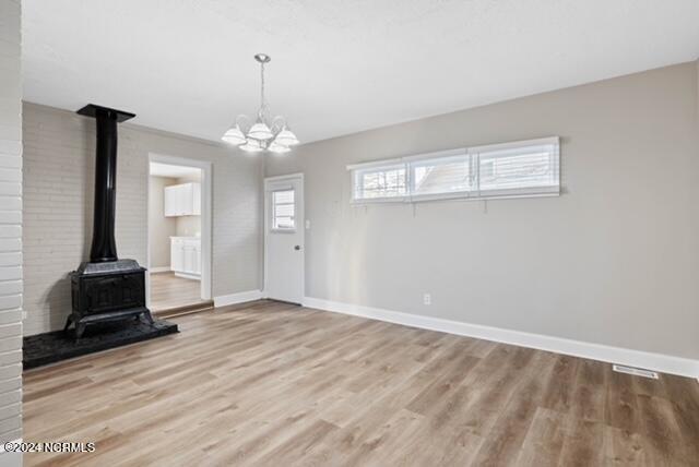 unfurnished living room with brick wall, a notable chandelier, a wood stove, and light wood-type flooring