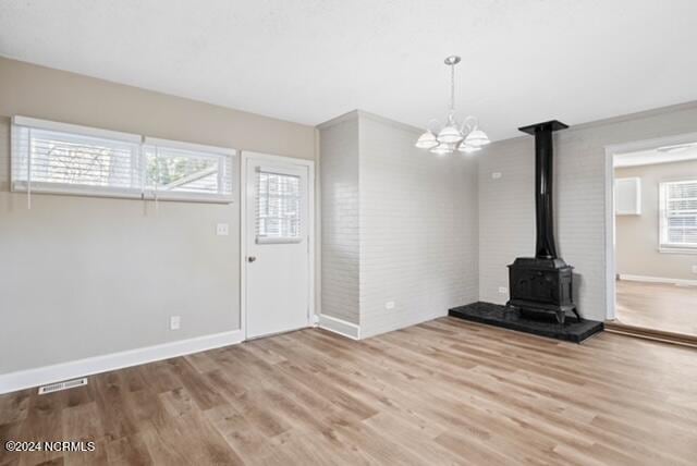 unfurnished living room with a notable chandelier, a wood stove, and light hardwood / wood-style flooring