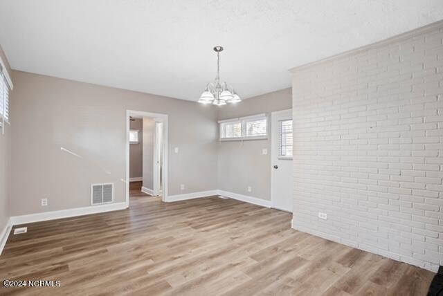 unfurnished room featuring brick wall, an inviting chandelier, and hardwood / wood-style floors