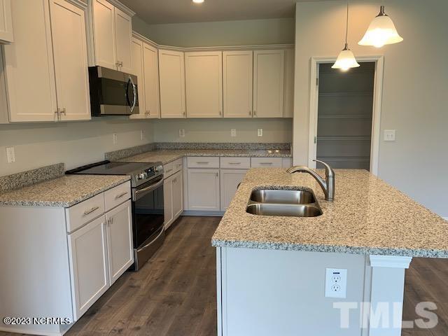 kitchen with appliances with stainless steel finishes, sink, dark wood-type flooring, a kitchen island with sink, and light stone countertops