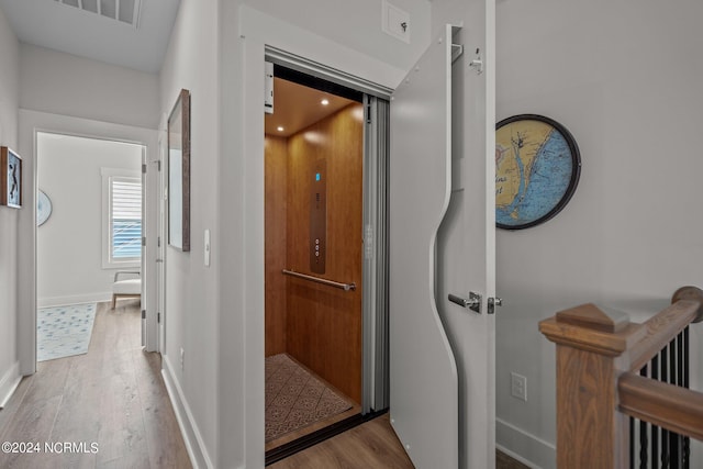 corridor with elevator and light hardwood / wood-style floors