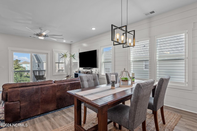 dining space featuring wood walls, wood-type flooring, and ceiling fan with notable chandelier