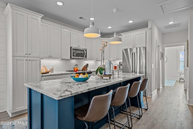 kitchen with white cabinets, an island with sink, pendant lighting, and stainless steel appliances