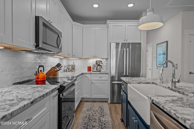 kitchen with appliances with stainless steel finishes, white cabinets, light stone counters, tasteful backsplash, and pendant lighting