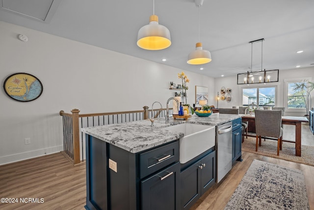 kitchen with light hardwood / wood-style flooring, pendant lighting, light stone counters, and a center island with sink