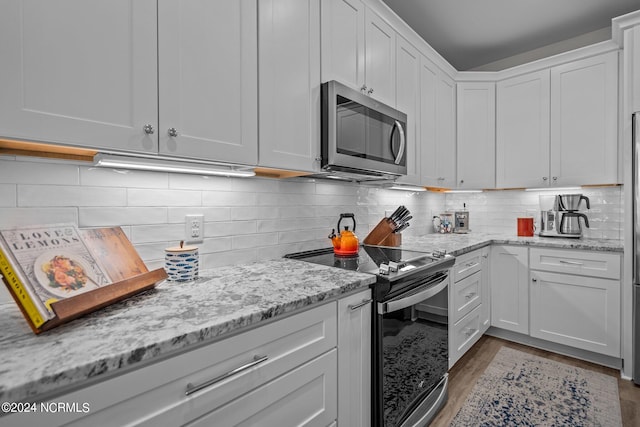 kitchen with light wood-type flooring, light stone counters, stainless steel appliances, backsplash, and white cabinets