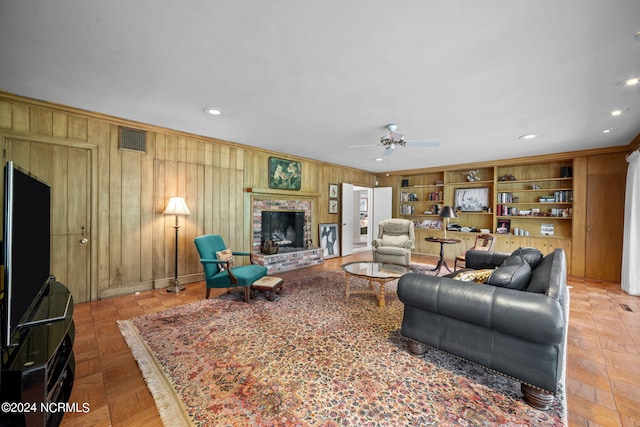 living room featuring wood walls, a brick fireplace, ceiling fan, light parquet flooring, and built in features