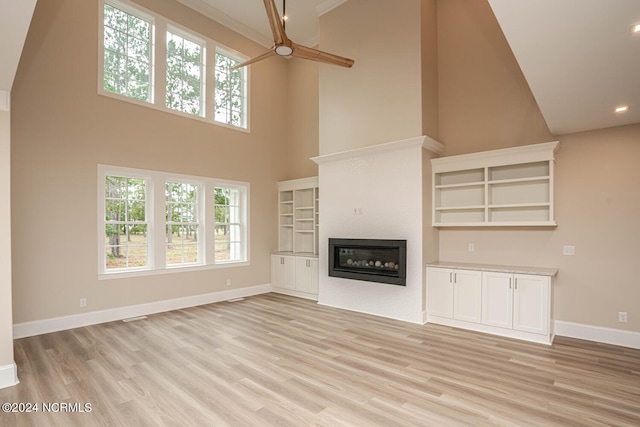 unfurnished living room featuring light wood finished floors, a glass covered fireplace, and a wealth of natural light