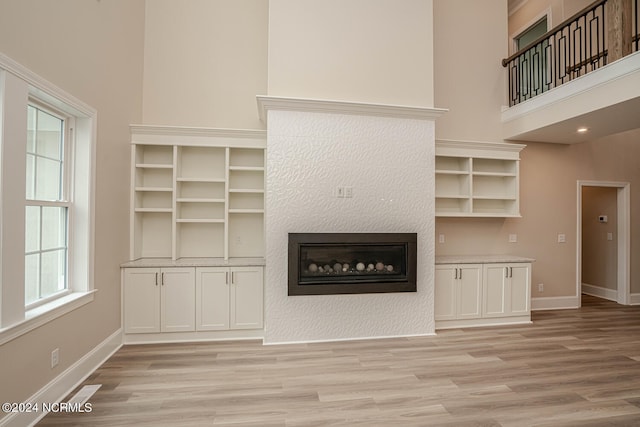 unfurnished living room featuring light wood-style floors, a high ceiling, baseboards, and a glass covered fireplace