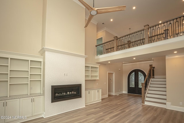 unfurnished living room with french doors, a towering ceiling, stairway, light wood-style floors, and a glass covered fireplace