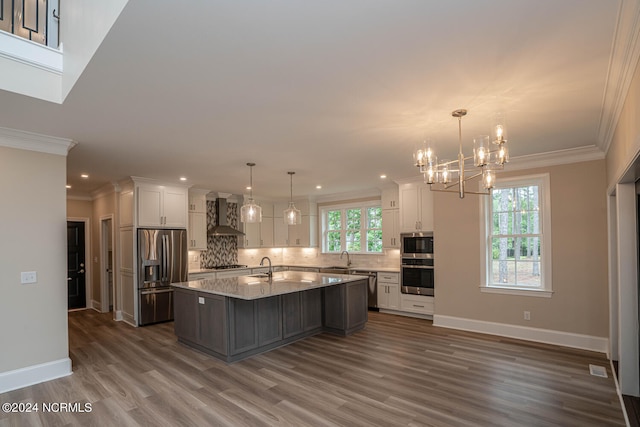 kitchen featuring decorative backsplash, dark wood-type flooring, wall chimney exhaust hood, an island with sink, and appliances with stainless steel finishes