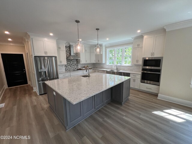 kitchen featuring stainless steel appliances, tasteful backsplash, a center island with sink, wall chimney range hood, and dark hardwood / wood-style flooring