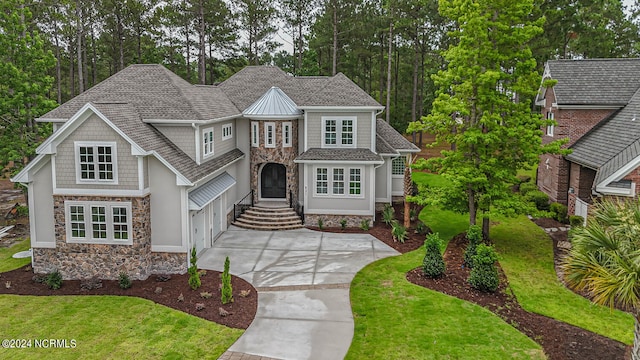 view of front of property featuring stone siding, a front lawn, concrete driveway, and roof with shingles