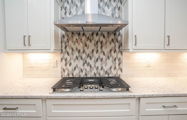 kitchen featuring wall chimney exhaust hood, stainless steel gas cooktop, white cabinets, and backsplash