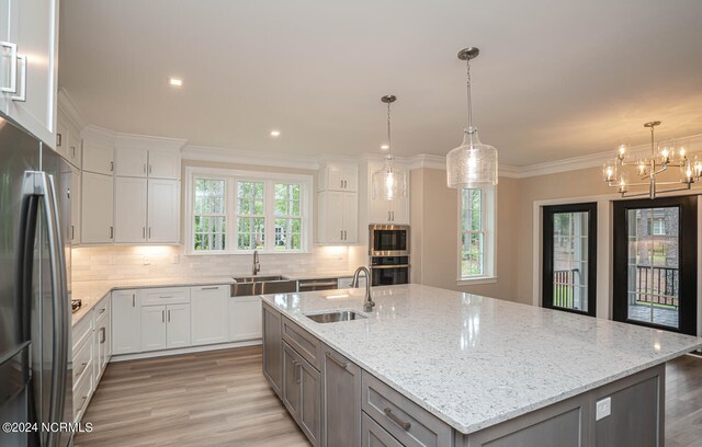 kitchen with light hardwood / wood-style floors, sink, decorative backsplash, and an island with sink