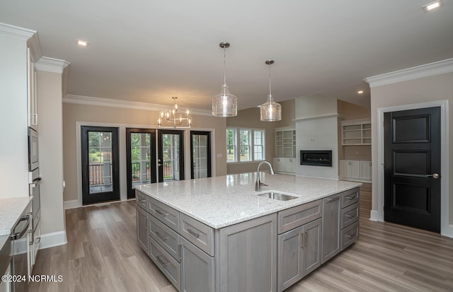 kitchen featuring light wood-type flooring, light stone counters, sink, decorative light fixtures, and a center island with sink