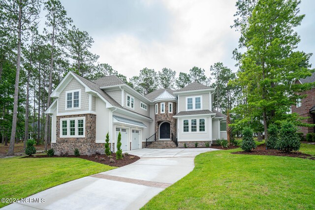 view of front of property with an attached garage, stone siding, a front lawn, and concrete driveway