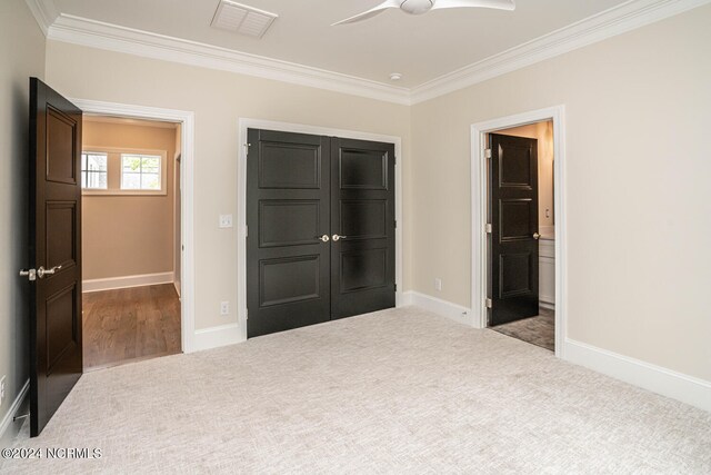 unfurnished bedroom with ceiling fan, carpet, crown molding, and a closet