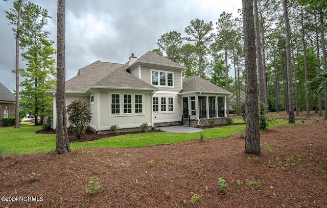 back of house with a patio, a sunroom, roof with shingles, a lawn, and a chimney