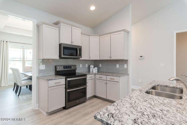 kitchen featuring appliances with stainless steel finishes, sink, backsplash, lofted ceiling, and light hardwood / wood-style flooring