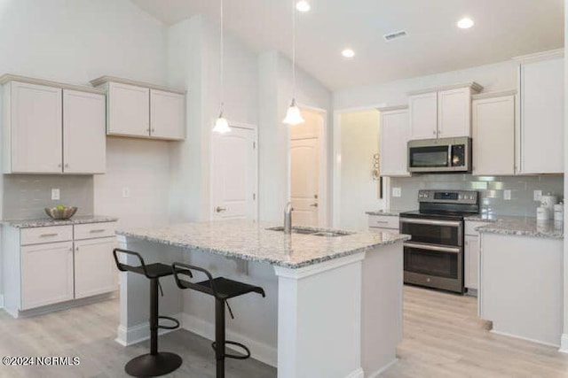 kitchen featuring appliances with stainless steel finishes, tasteful backsplash, light wood-type flooring, hanging light fixtures, and a kitchen island with sink