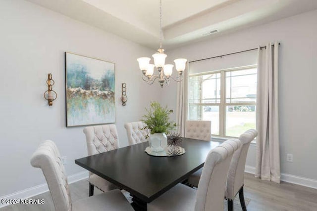 dining area with wood-type flooring, a notable chandelier, and a tray ceiling