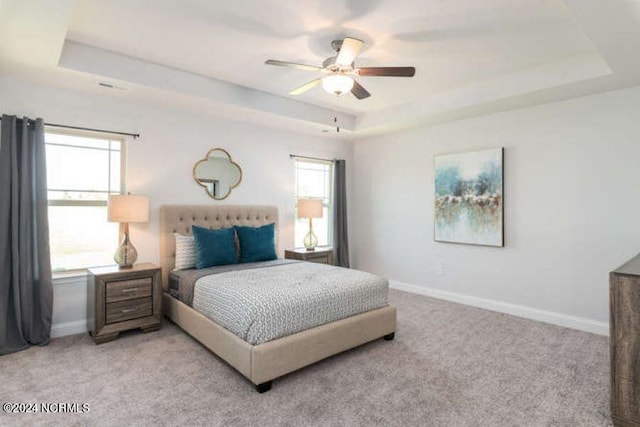 carpeted bedroom with ceiling fan and a tray ceiling