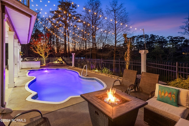 pool at dusk featuring a patio area and an outdoor living space with a fire pit