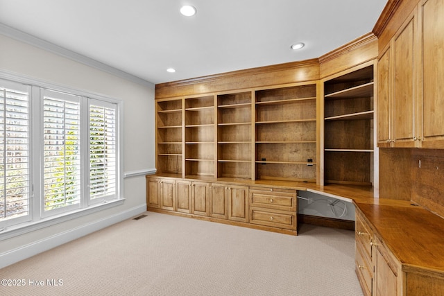 unfurnished office featuring crown molding, built in desk, and light colored carpet