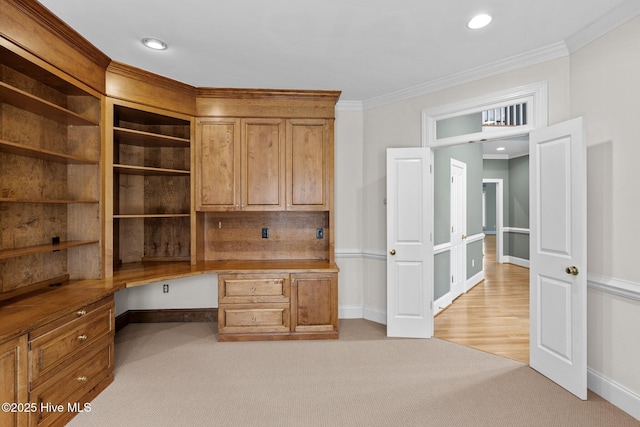 unfurnished office featuring ornamental molding, built in desk, and light carpet