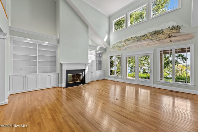 unfurnished living room featuring light wood-type flooring, crown molding, built in shelves, and a towering ceiling